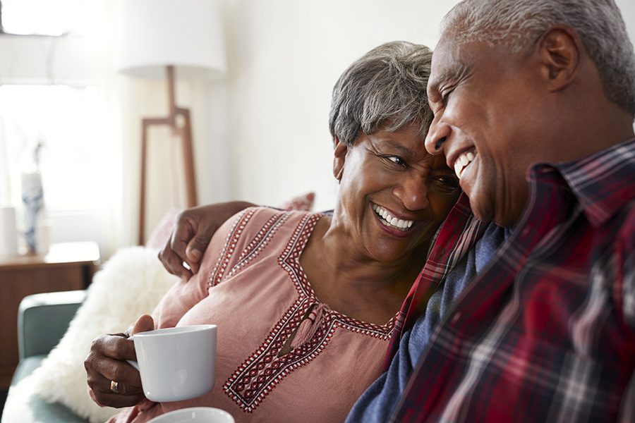 Medicare - Loving Couple Sitting on the Sofa at Home Relaxing with a Hot Drink