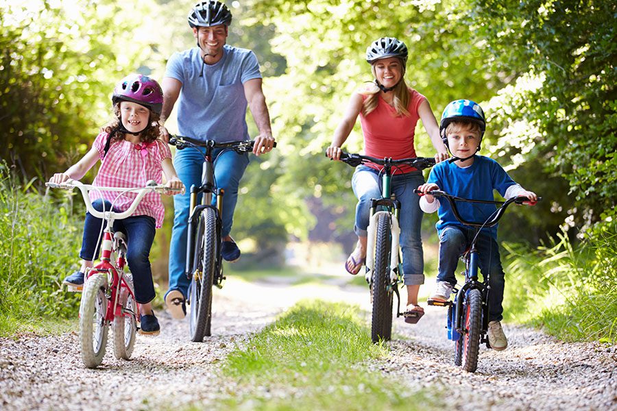 Employee Benefits - A Happy Family of Four Are Riding Their Bikes on a Dirt Road in the Countryside on a Sunny Day