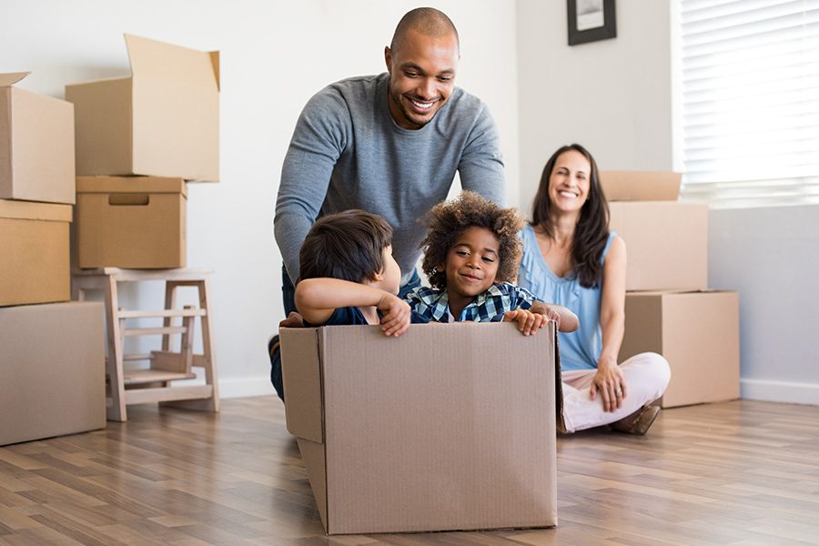 Personal Insurance - A Father Playing and Pushing His Children in a Box on the Floor on Moving Day While His Wife Watches and Smiles